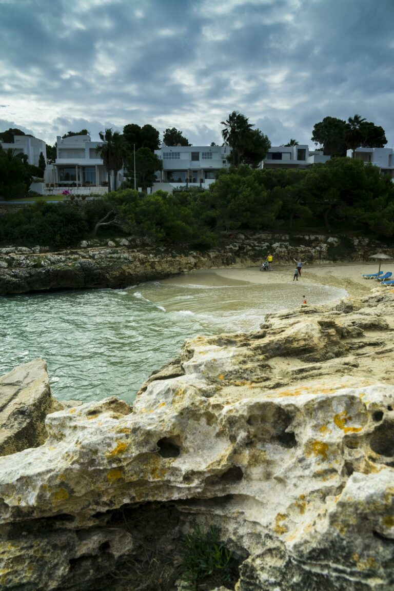 Idyllic coastal scene with rocky shoreline, sandy beach, and modern houses.